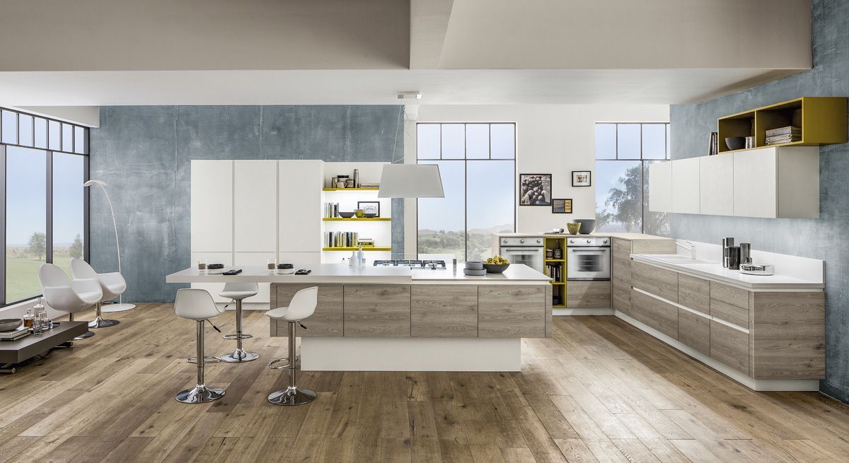 Cucina e soggiorno moderni a pianta aperta con isola, mobili bianchi, pavimenti in legno e ampie finestre.