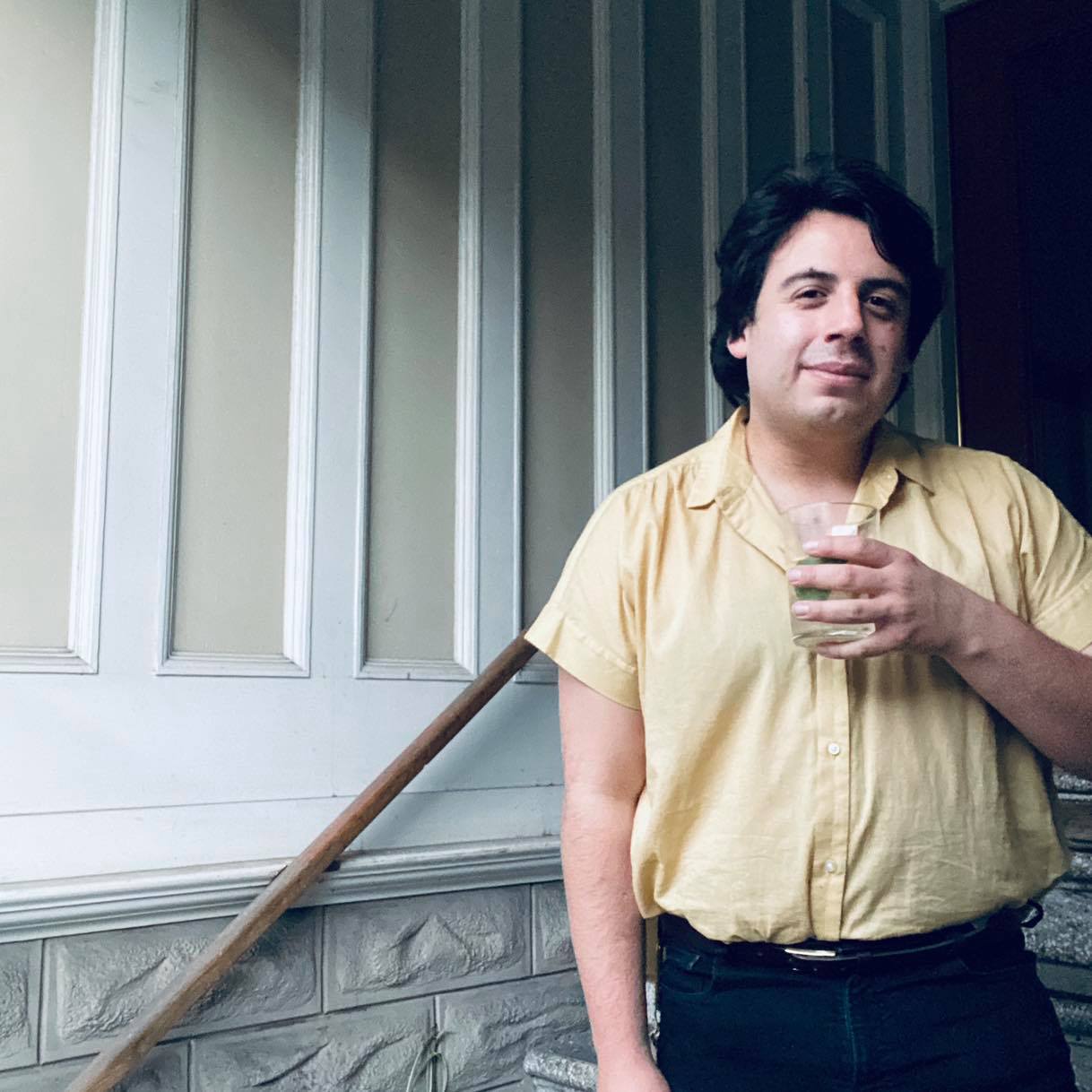 A man in a yellow shirt is holding a glass in his hand.