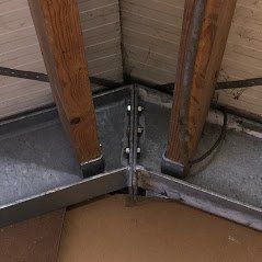 Een close-up van een metalen hoekverbinding die twee houten draagbalken in een constructie met elkaar verbindt.