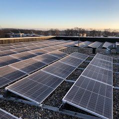 Rijen zonnepanelen geïnstalleerd op een plat, met grind bedekt dak onder een heldere, zonnige hemel.