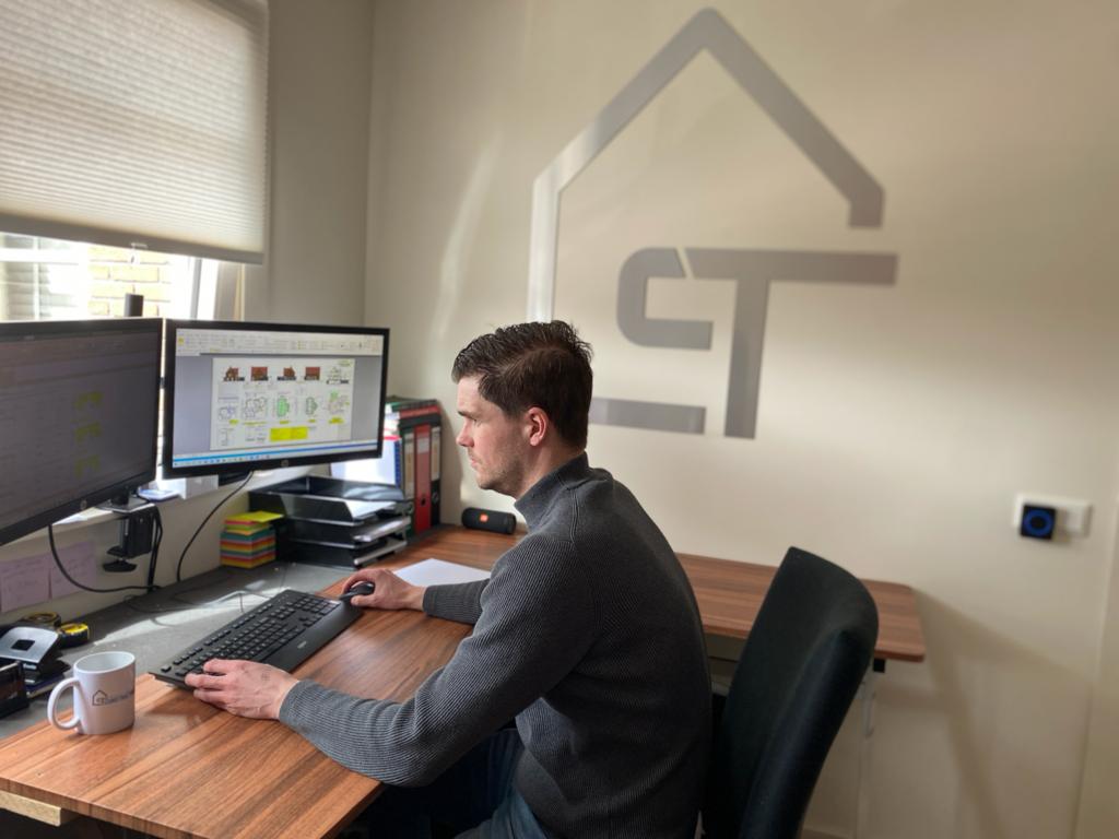 Iemand zit aan een bureau in een thuiskantoor en typt op een toetsenbord voor twee computermonitoren.