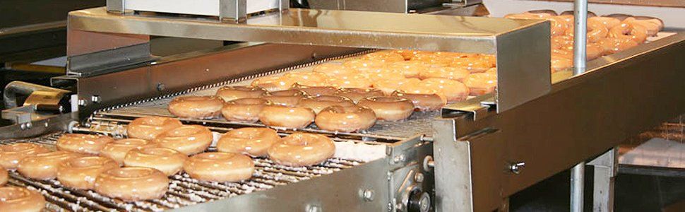 Donuts moving along a conveyor belt, possibly in a bakery or food production facility.