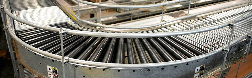 Curving conveyor belt with metal rollers, part of an industrial automated system.