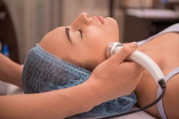 Close-up portrait of a young woman with a towel on her head lying on a table with closed eyes getting a laser skin treatment in healthy beauty spa salon
