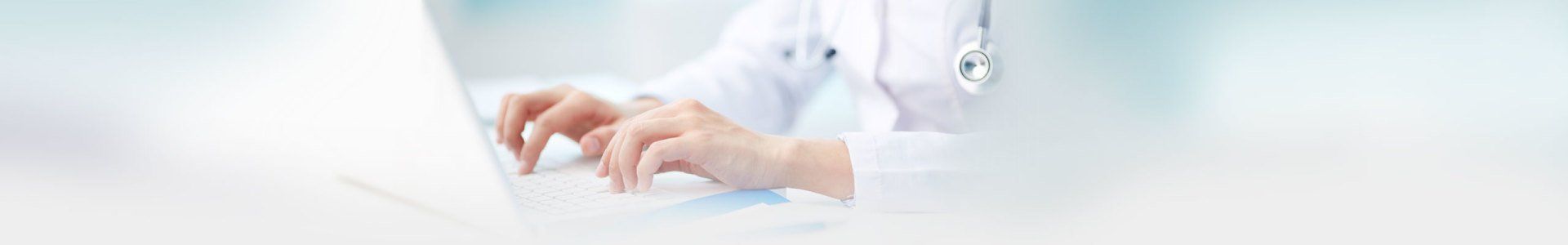 Doctor typing on a laptop, close-up of hands and white lab coat.