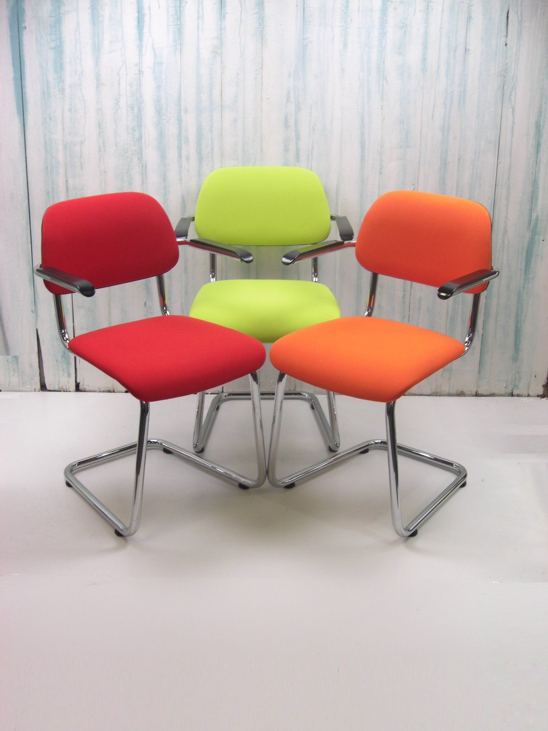 Vier kleurrijke stoelen met chromen frames: rood, groen en oranje. Opgesteld in een halve cirkel.