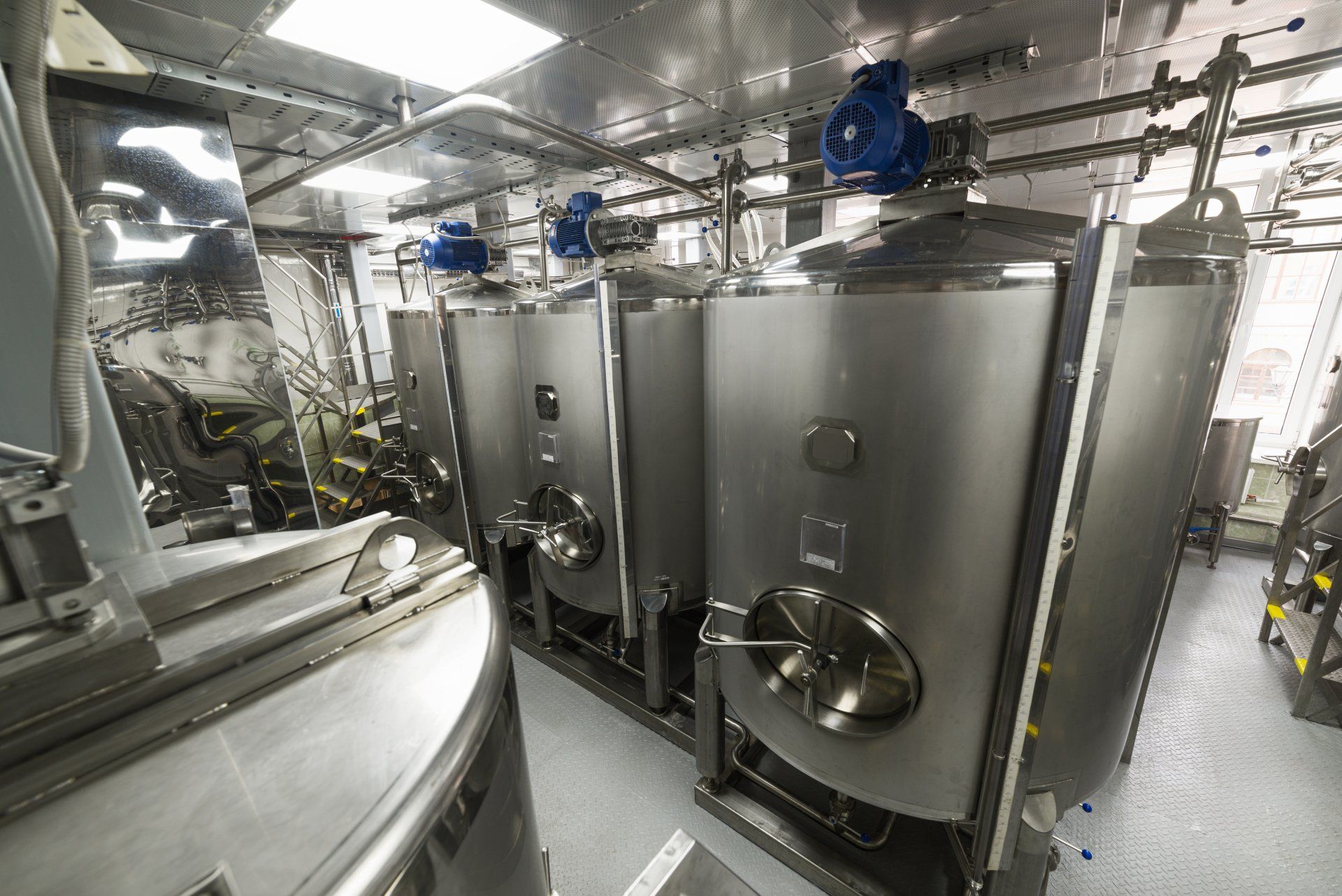 A row of stainless steel tanks are lined up in a room.