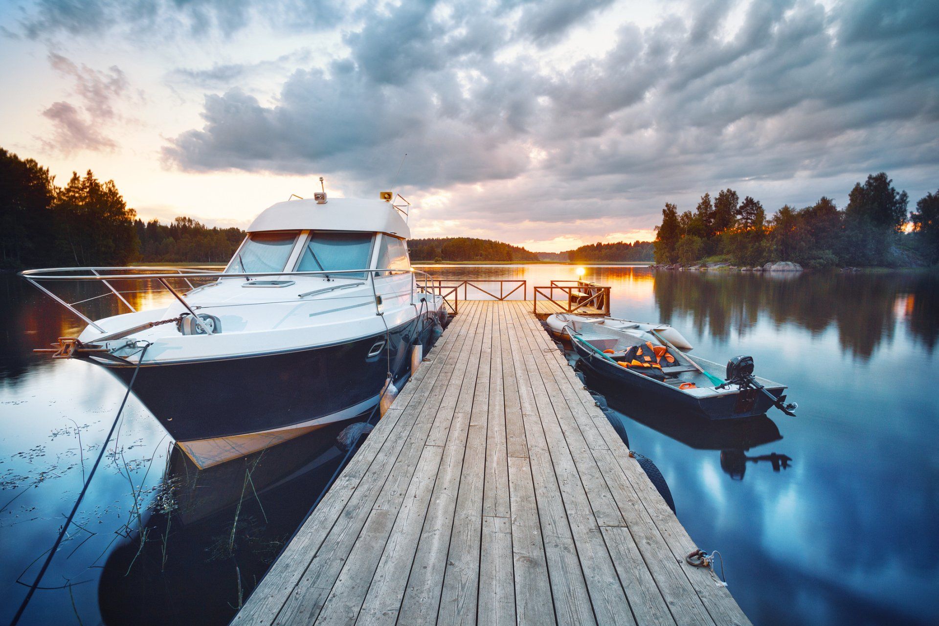 Boat docked on a wooden pier at sunset; cloudy sky reflects on the calm water.