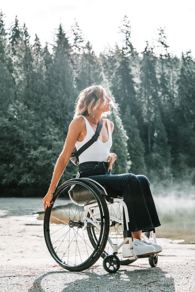 A woman in a wheelchair is sitting next to a lake.