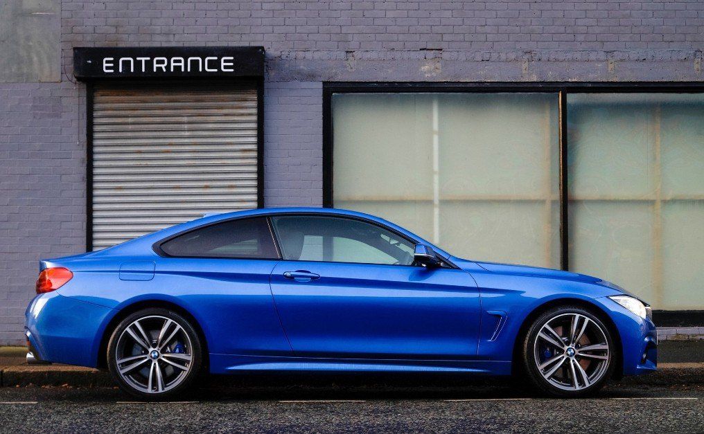 Blue BMW coupe parked in front of a gray brick building with an