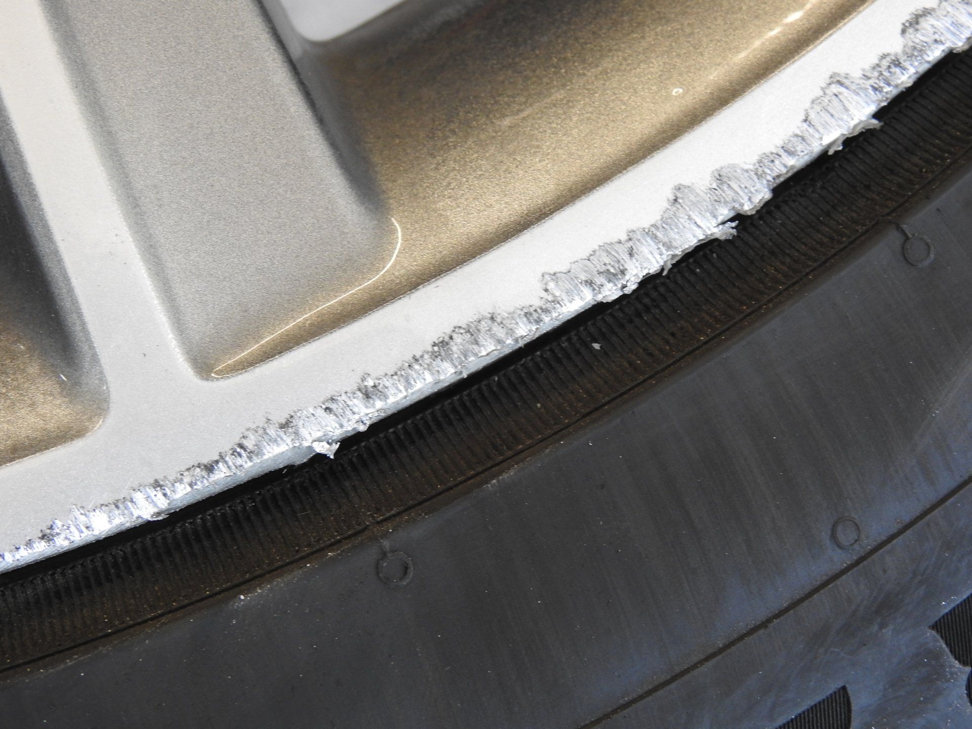 Close-up of a damaged silver car rim with peeling silver paint and a black tire.