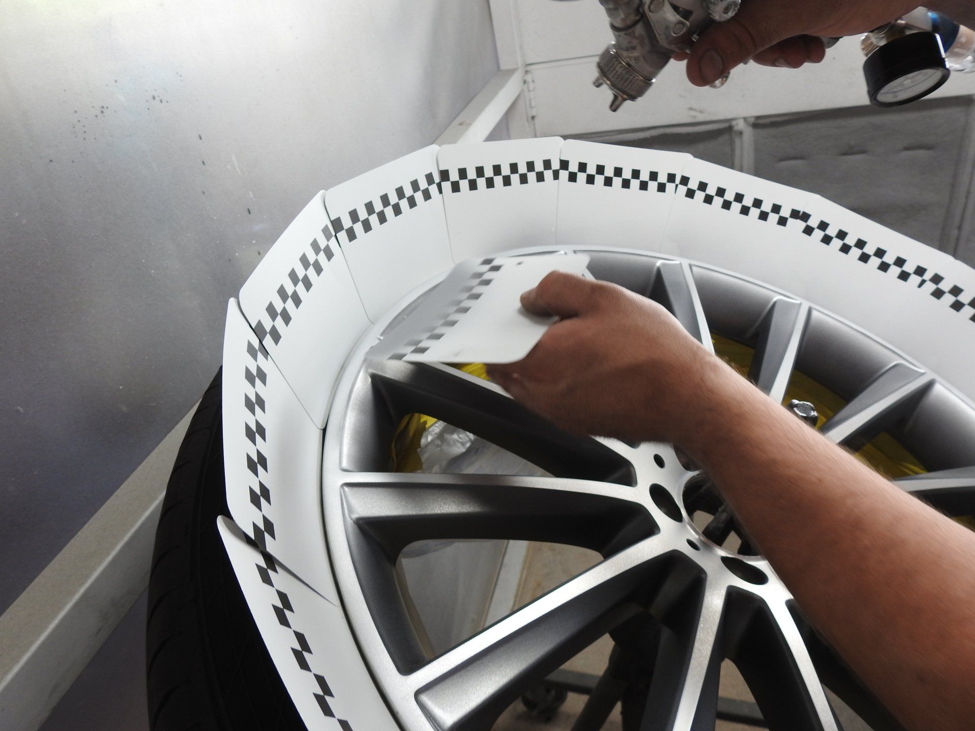 Person sprays a car wheel with paint. The wheel is masked with checkered tape.