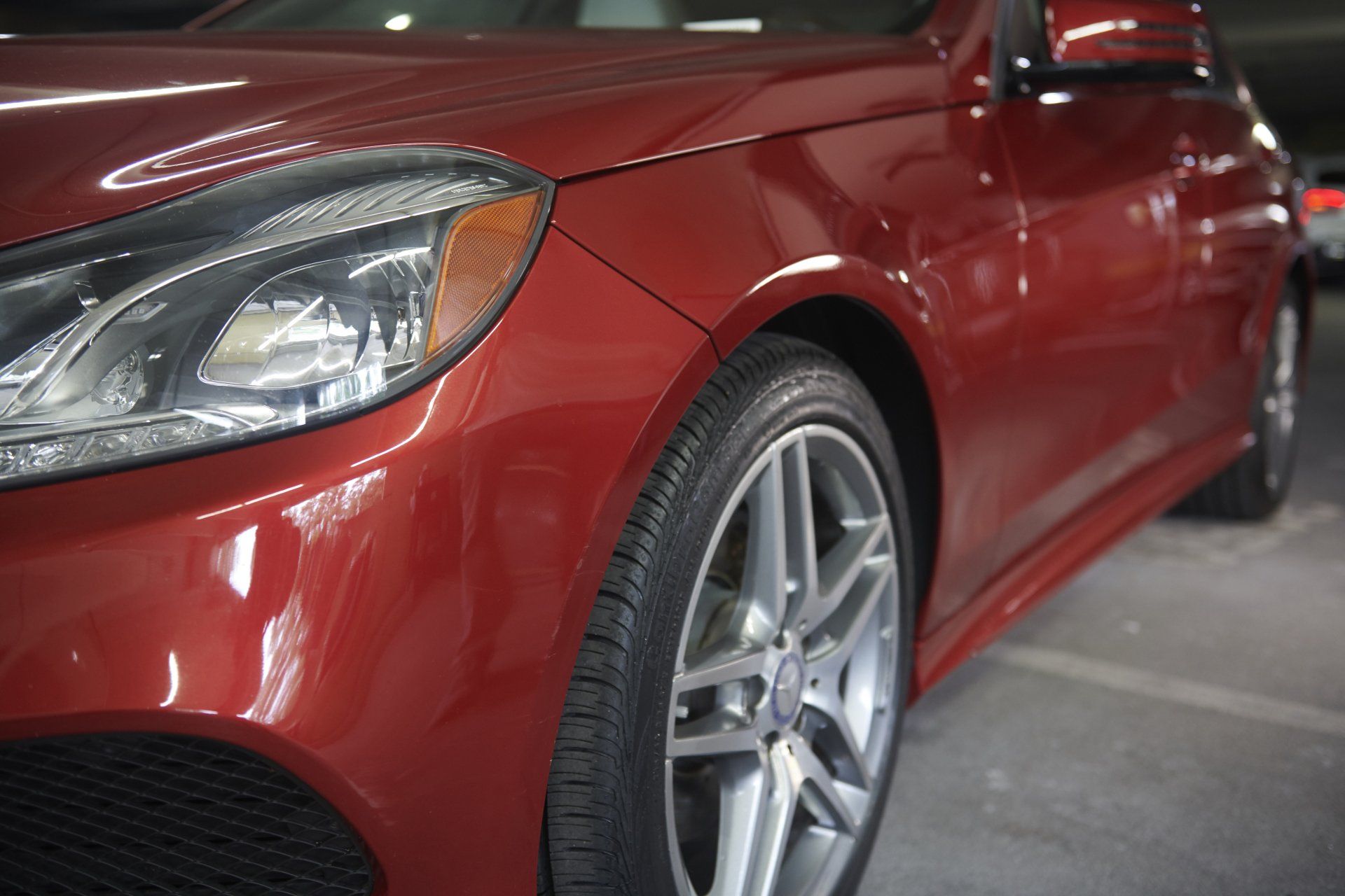Red Mercedes-Benz car parked inside a parking garage; front side view of the vehicle's details.