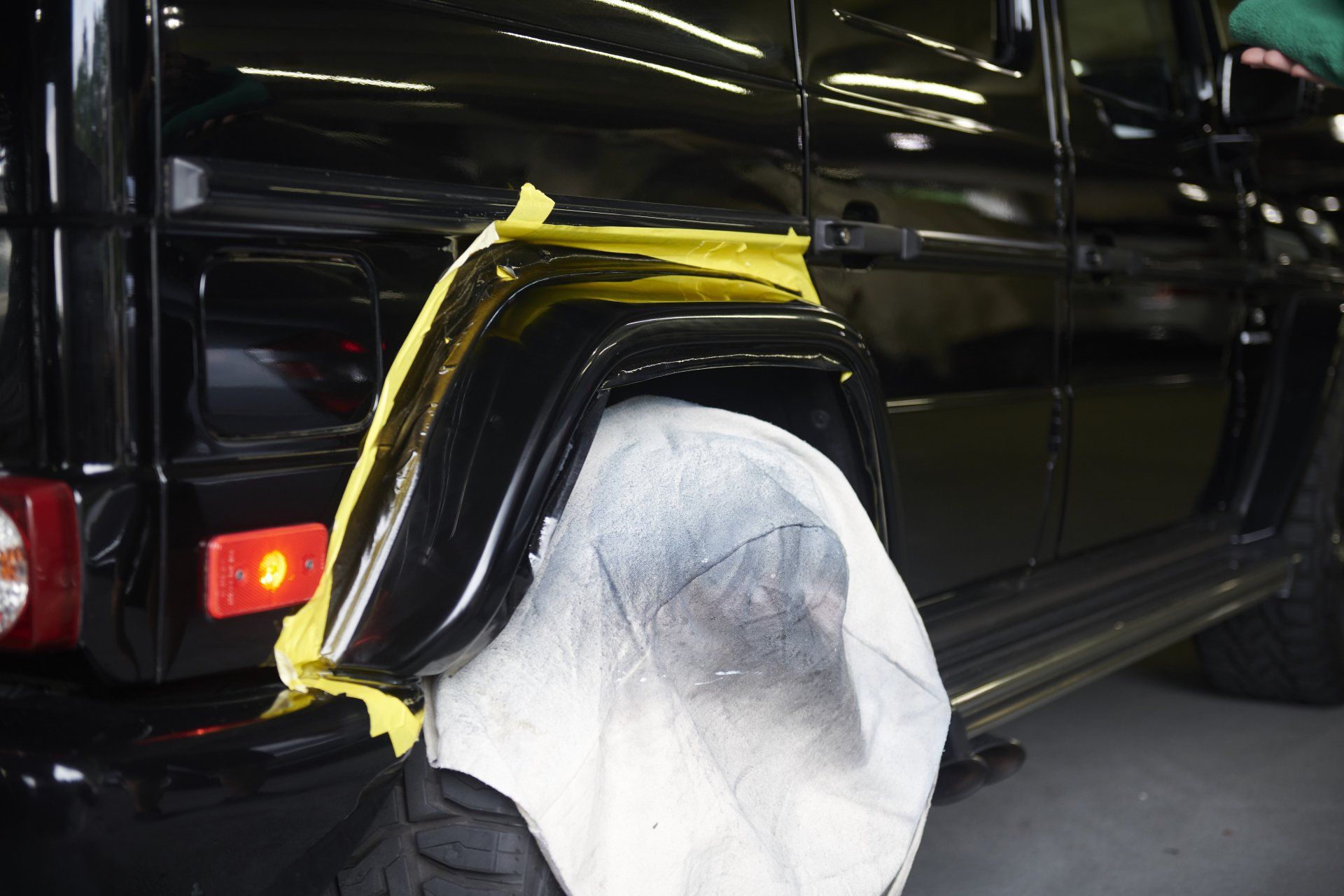 Black SUV being painted; fender area masked with yellow tape and covered with paper.