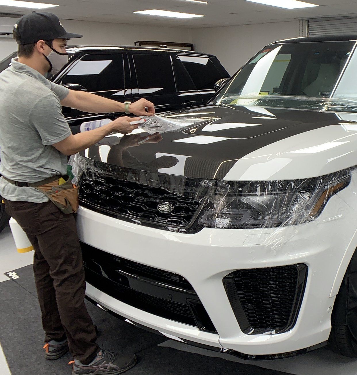 A person applying Xpel protective film to the hood of a white SUV with a carbon fiber hood.