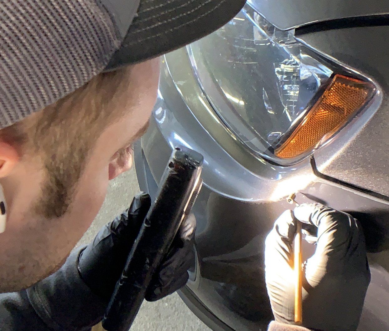 Person wearing gloves examines car headlight with a flashlight, likely repairing it.