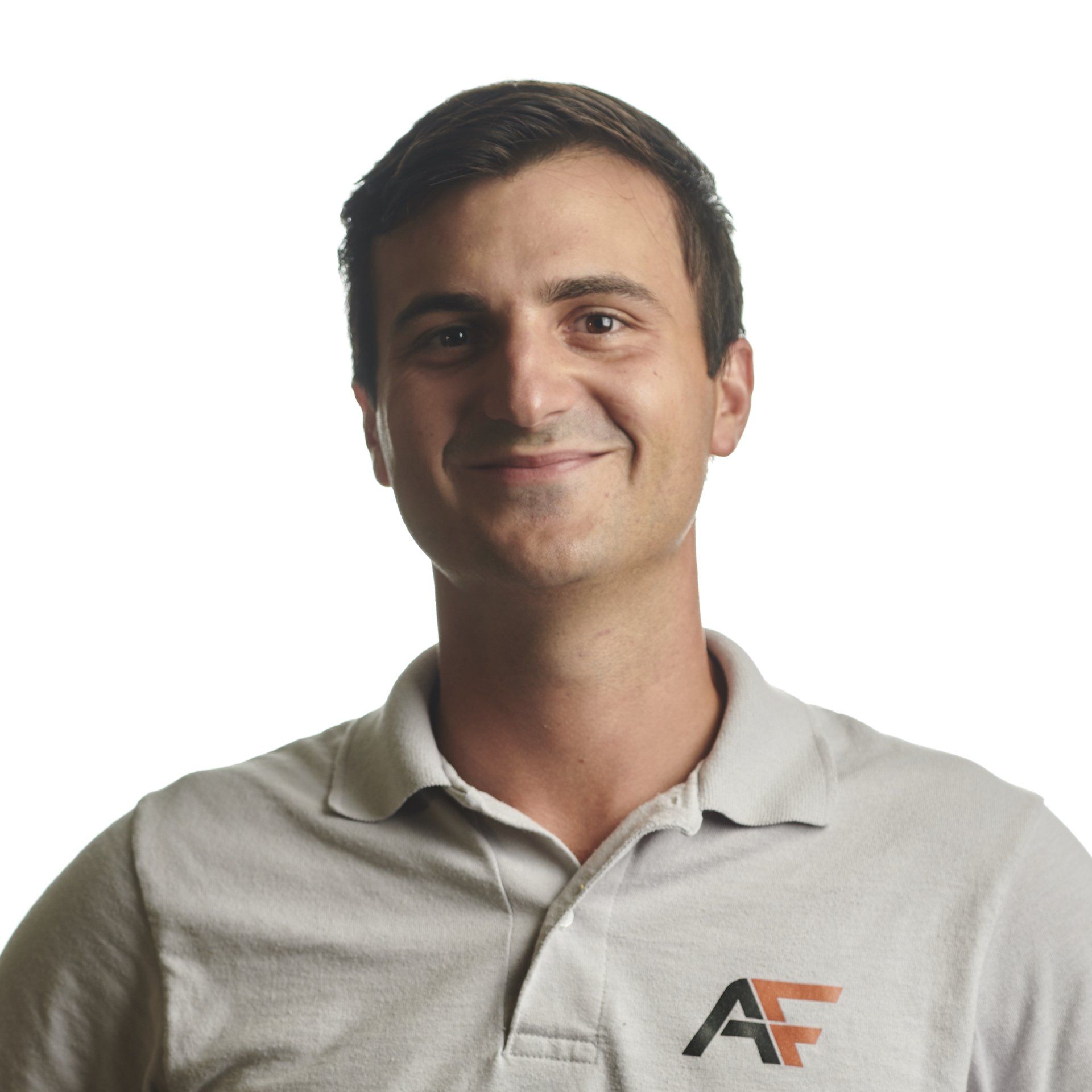 Man in a gray polo shirt smiles at the camera against a white background. Shirt has black logo.