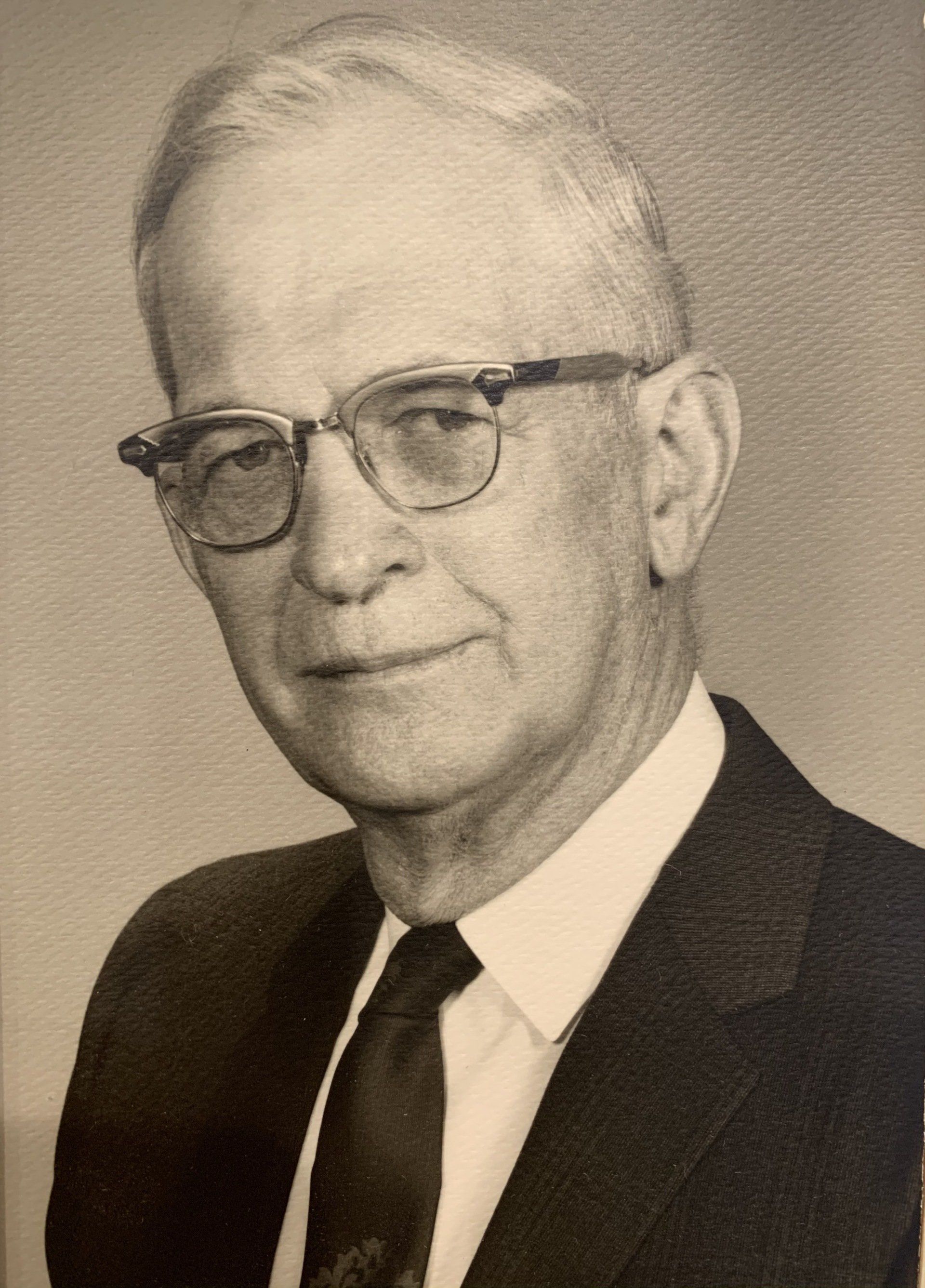 A man with glasses in a suit and tie, likely a formal portrait.