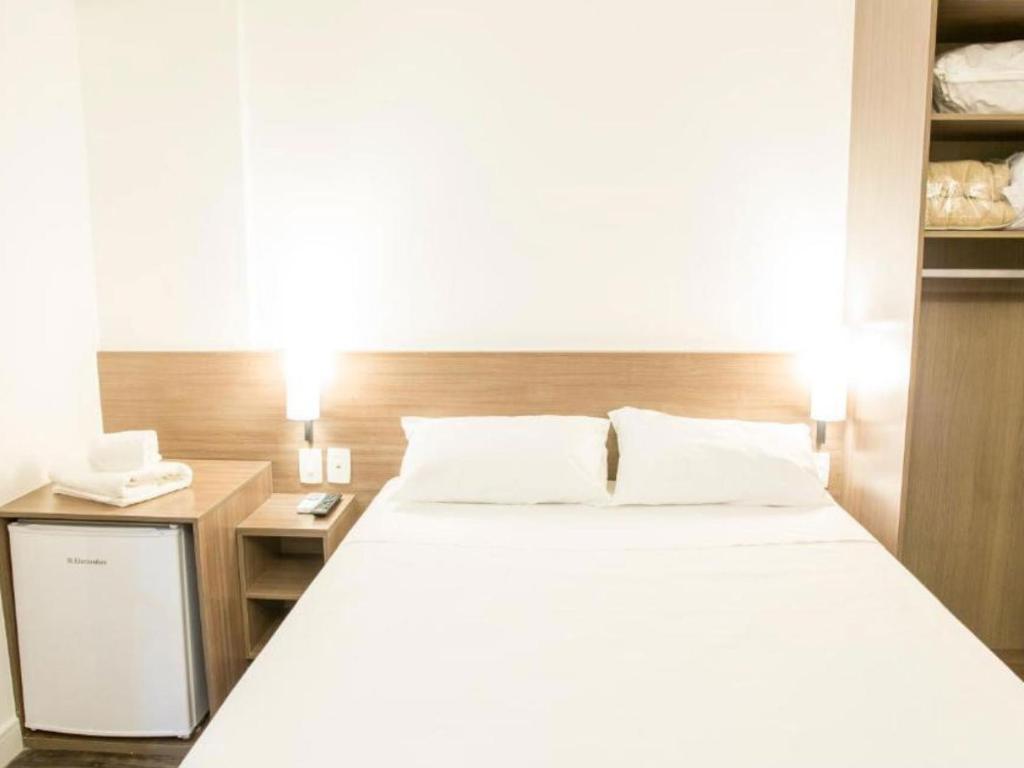 Um quarto de hotel com uma cama, mesa de cabeceira e geladeira.