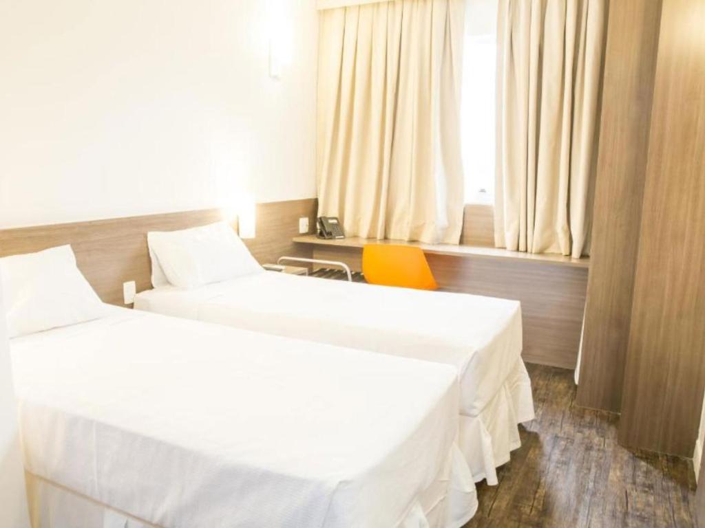 Um quarto de hotel com duas camas, uma escrivaninha e uma janela.
