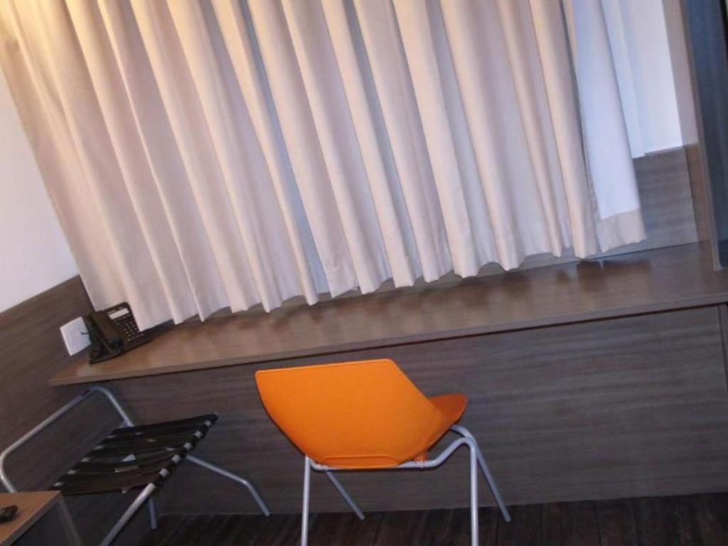 Uma cadeira laranja fica em frente a uma janela em um quarto de hotel