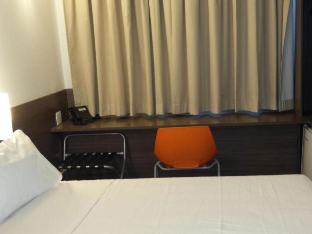 Um quarto de hotel com uma cama, uma escrivaninha e uma cadeira laranja