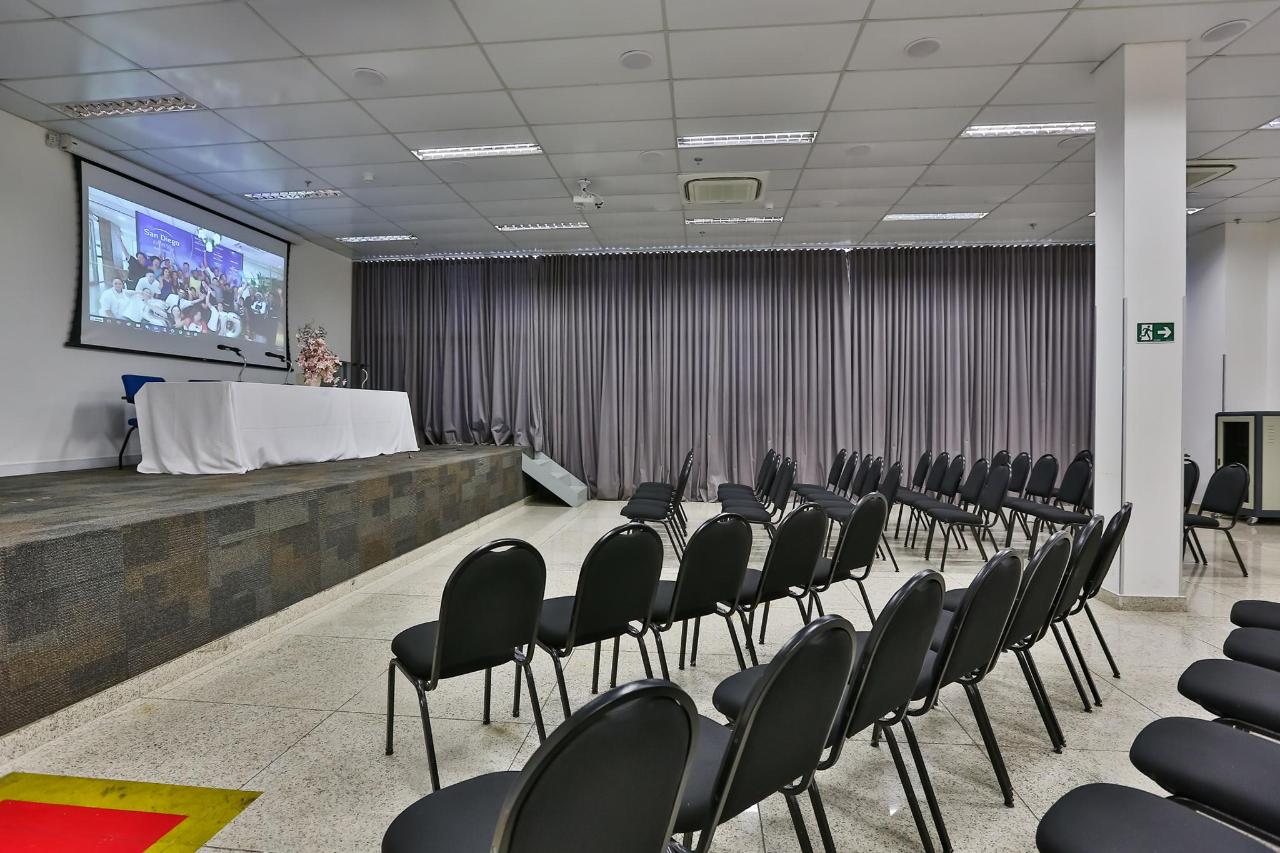 Uma sala grande com fileiras de cadeiras e uma tela de projetor.