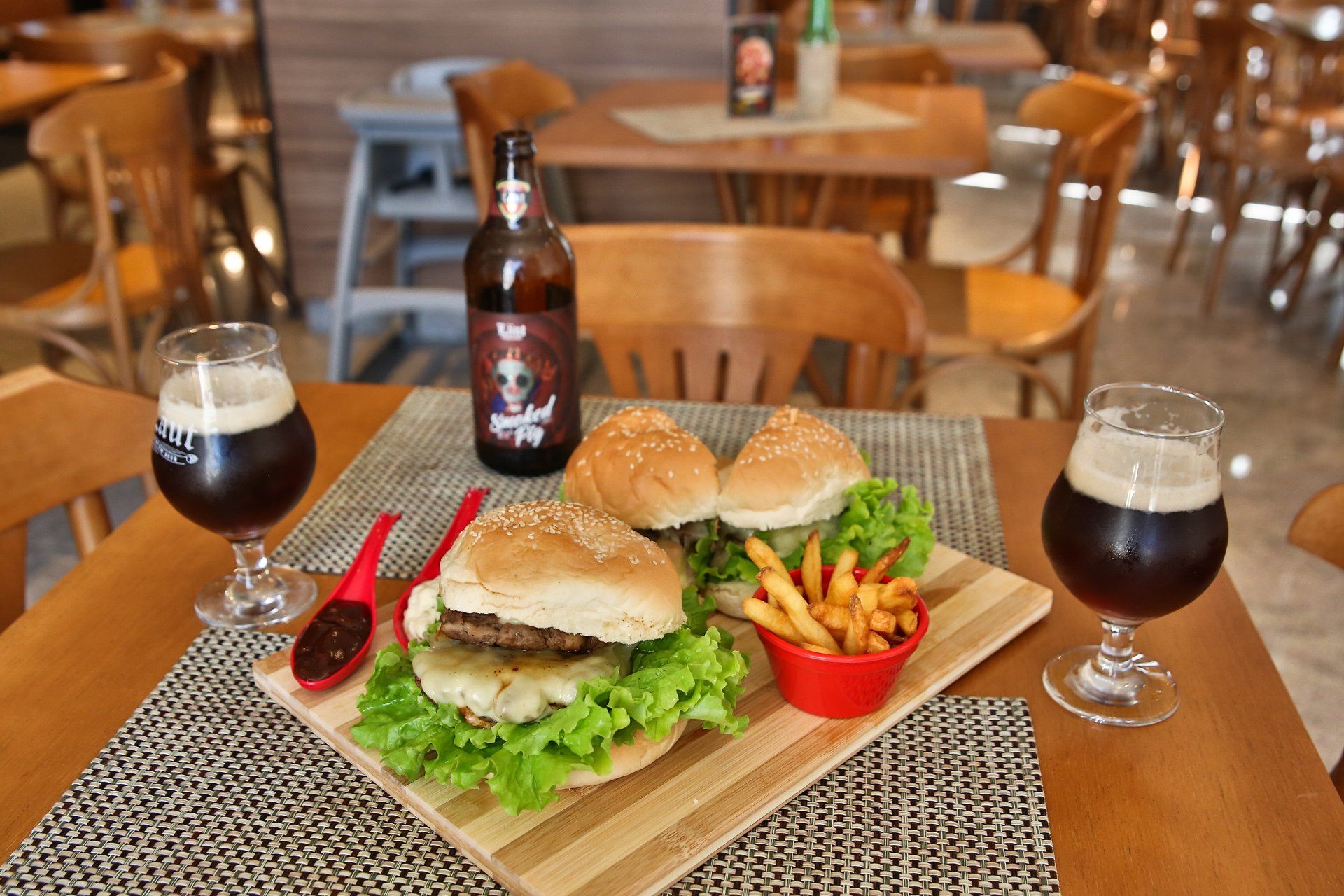 Um hambúrguer e batatas fritas estão em uma tábua de madeira ao lado de uma garrafa de cerveja.