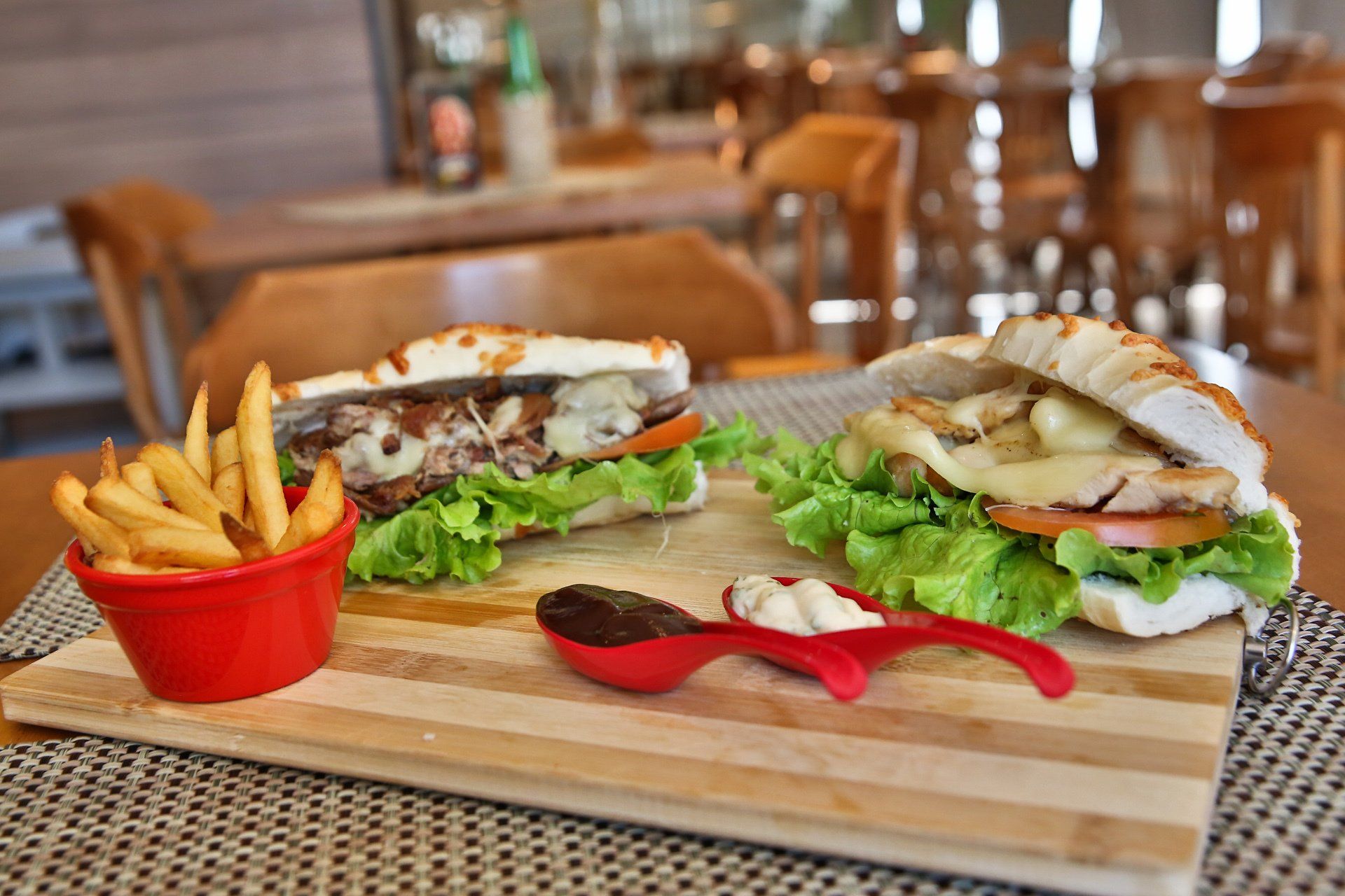 Dois sanduíches e batatas fritas em uma tábua de corte de madeira sobre uma mesa.