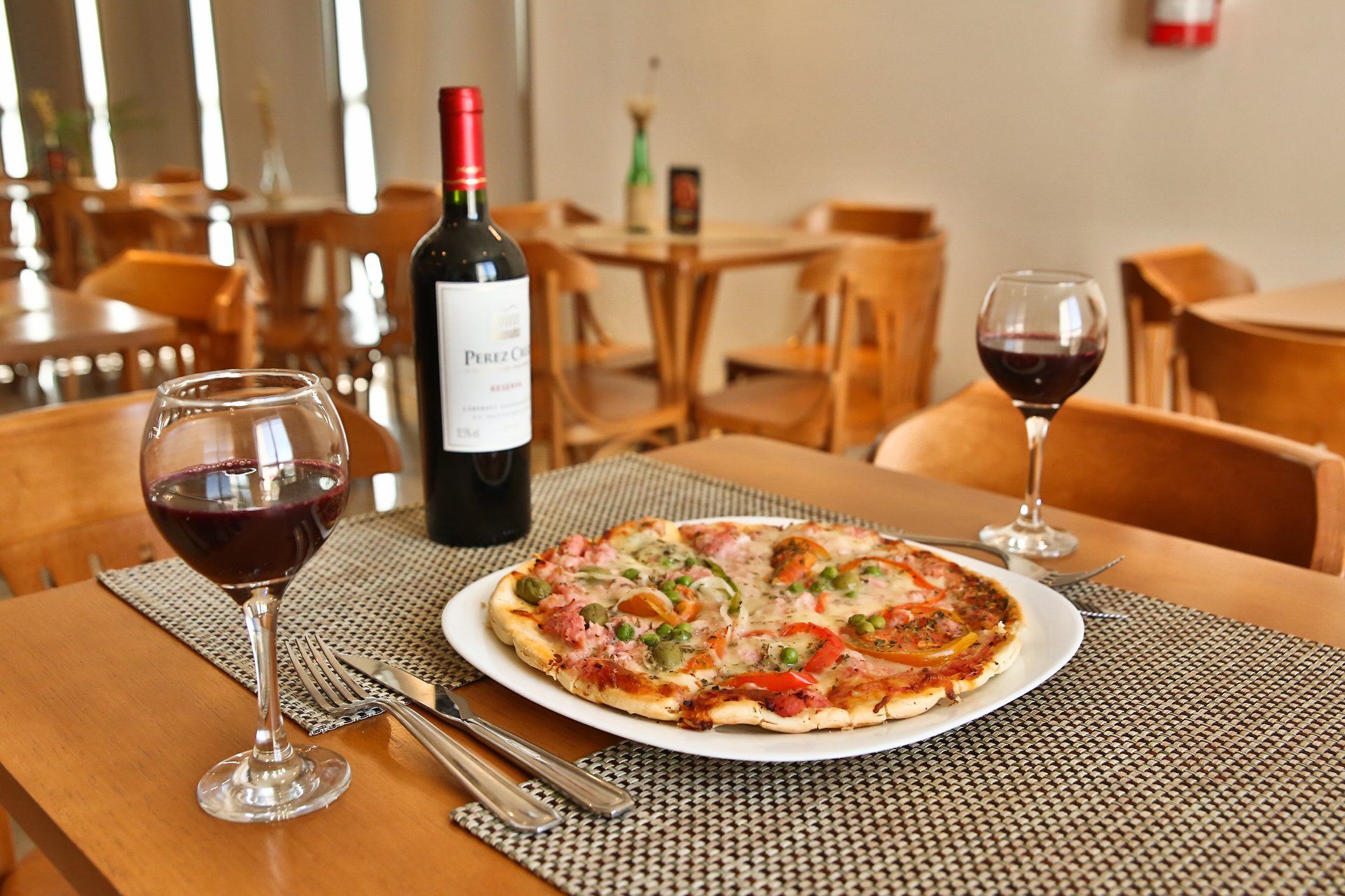 Uma pizza e uma taça de vinho estão sobre uma mesa.