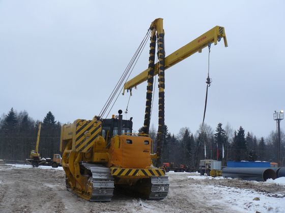 Yellow tracked crane lifting a vertical pile foundation in a snowy construction site