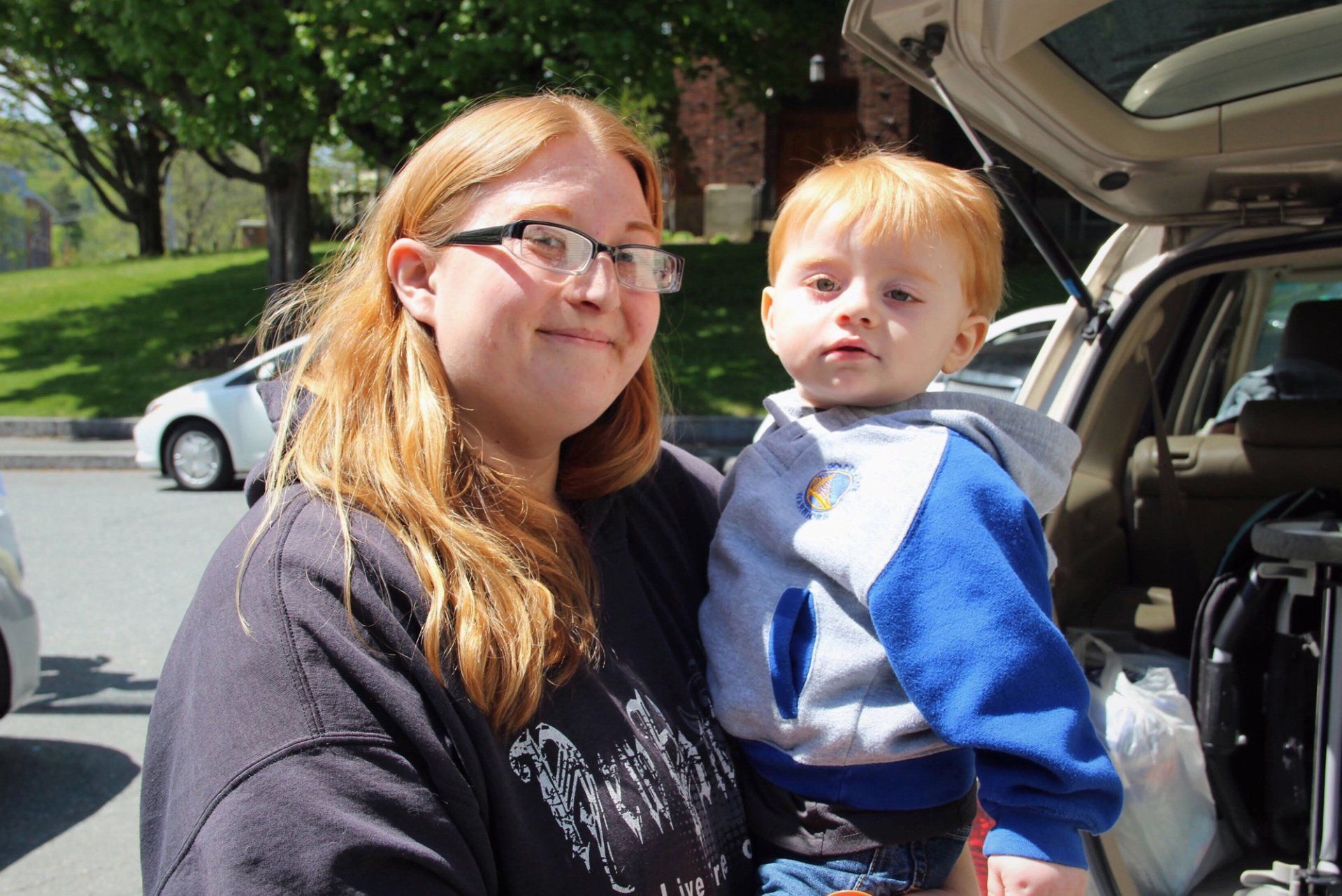 A woman is holding a baby in front of a car