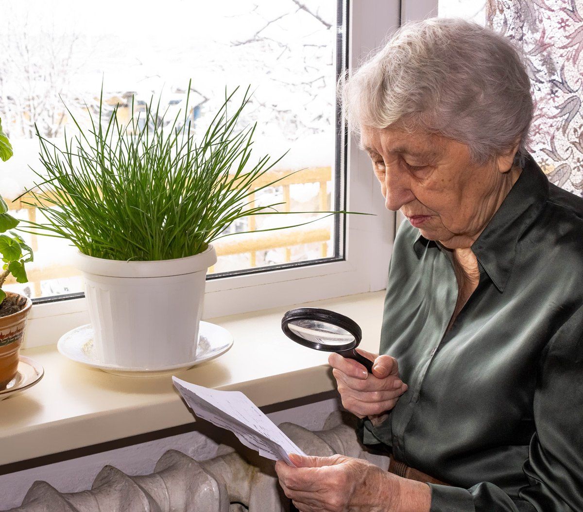 An elderly woman is reading a book with a magnifying glass.