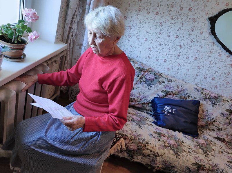 An elderly woman is sitting on a couch reading a piece of paper