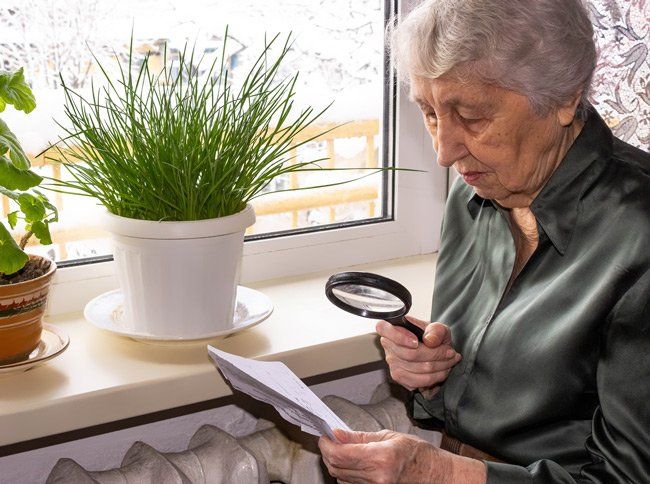 An elderly woman is looking through a magnifying glass at a piece of paper.