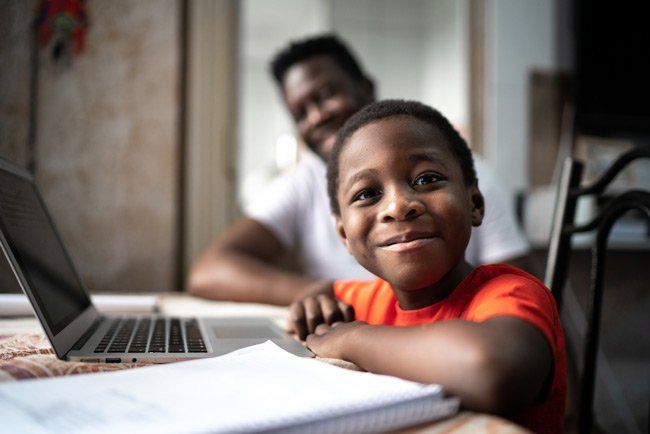 A young boy is sitting at a table with a laptop and a notebook.