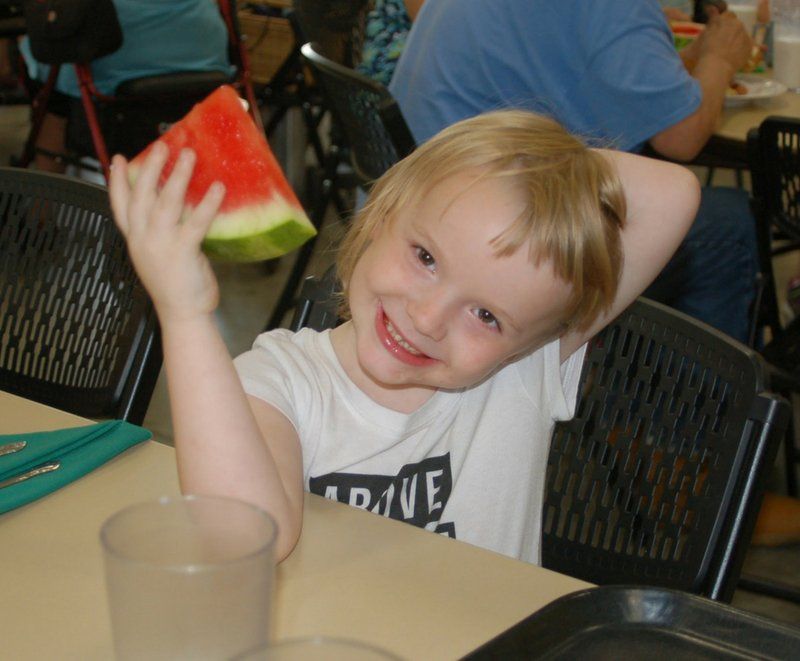 A little girl holding a slice of watermelon and wearing a shirt that says dave