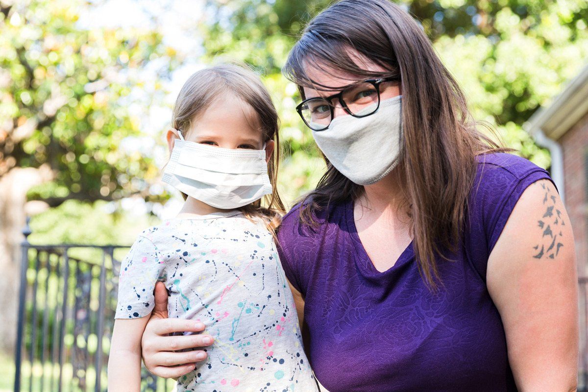A woman is holding a little girl wearing a face mask.