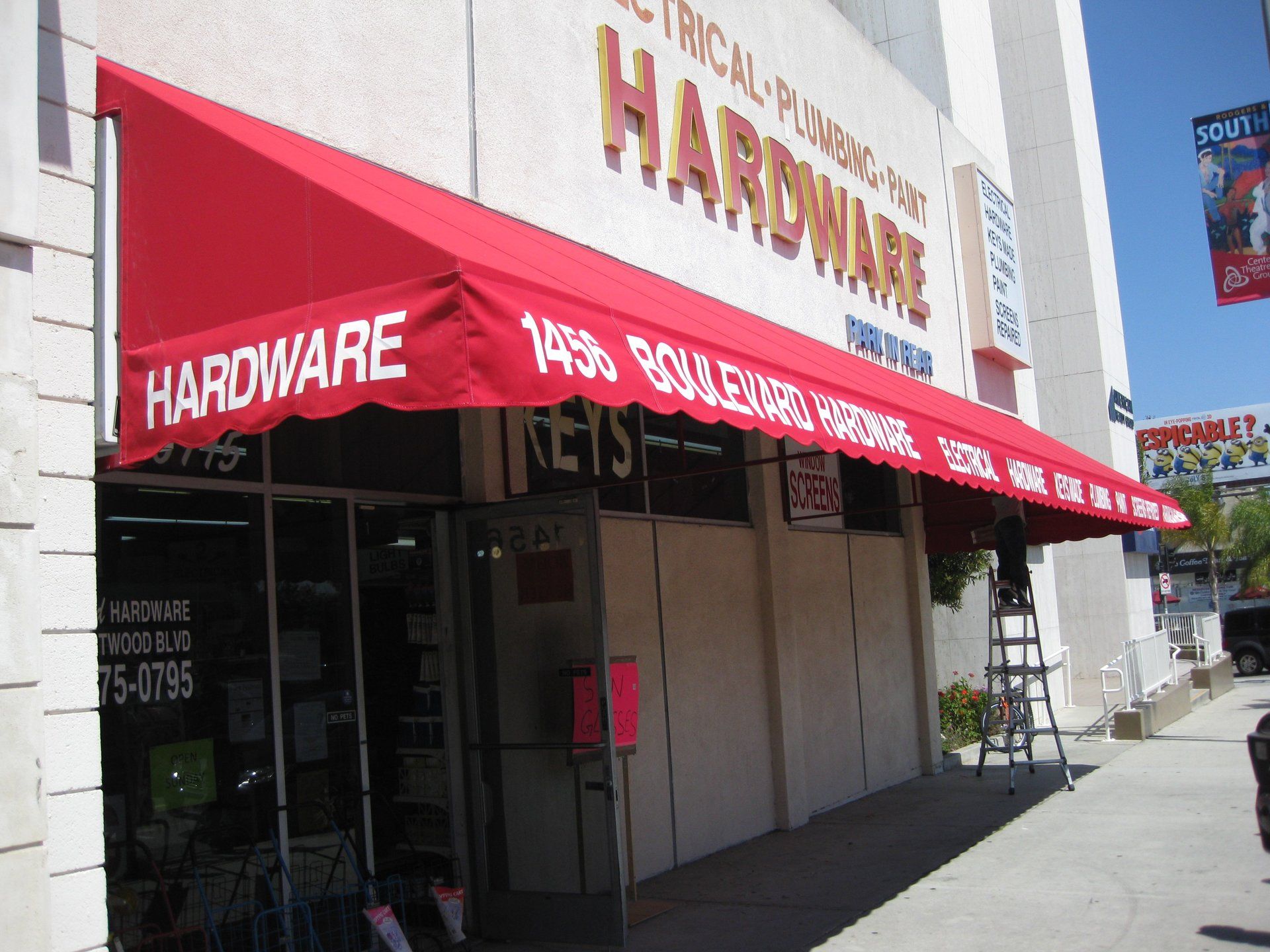 Storefront with red awning reading “Hardware” on a sunny street corner