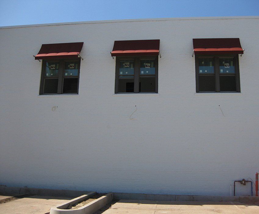 White building wall with three small windows topped by red awnings under a blue sky