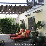 Patio with red lounge chairs under a pergola beside a cream house and greenery