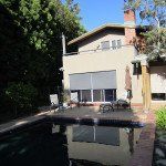Modern house with a pool and lounge chairs beside a tree-lined driveway