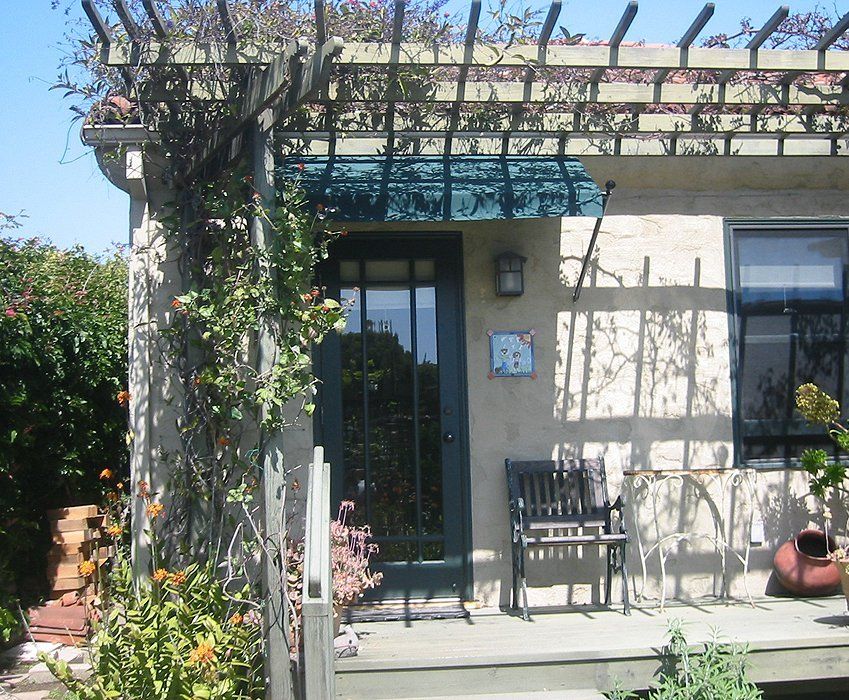 Small courtyard patio with a glass door, pergola, chair, and potted plants in sunlight