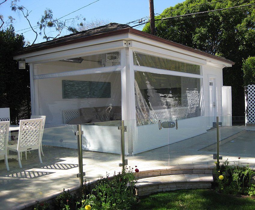 White screened porch/sunroom with red roof in a garden, with patio chairs and railing in front.