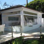 White gazebo-style patio on a sunlit deck with mesh screens and surrounding greenery