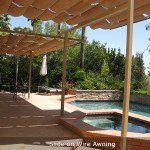 Wooden pergola shading a patio beside a pool and hot tub, with greenery beyond