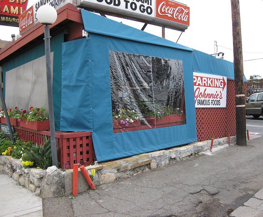 Small roadside food stand with blue tarp walls and a parking sign beside a Coca-Cola to-go sign.
