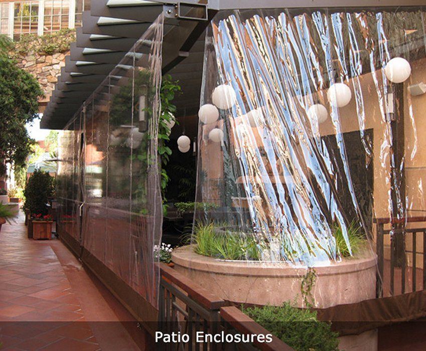 Patio enclosure with clear vinyl curtains and hanging string lights along a brick walkway