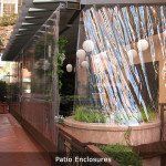 Covered patio enclosure with clear panels, hanging string lights, and potted greenery beside a walkway
