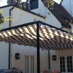 Pergola with striped shadows on a modern house patio under a dark roof